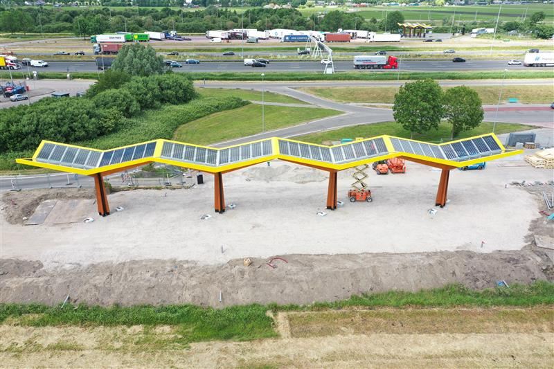 Snellaadstation onder een langgerekte solar carport langs de snelweg, tijdens de bouw