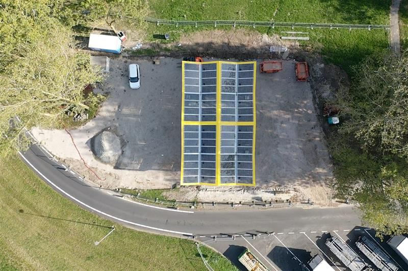 Solar carport van bovenaf: twee vlakken lichtdoorlatende panelen in een geel frame, naast de weg