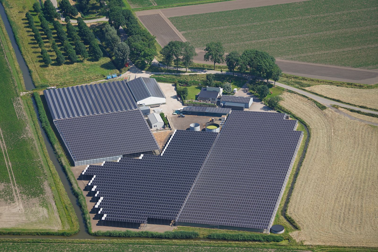 Luchtfoto van een tuinbouwbedrijf in de polder met zonnepanelen op kassen en schuren
